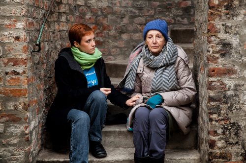 Ältere Frau sitzt mit Diakonie-Mitarbeiterin auf einer Stiege